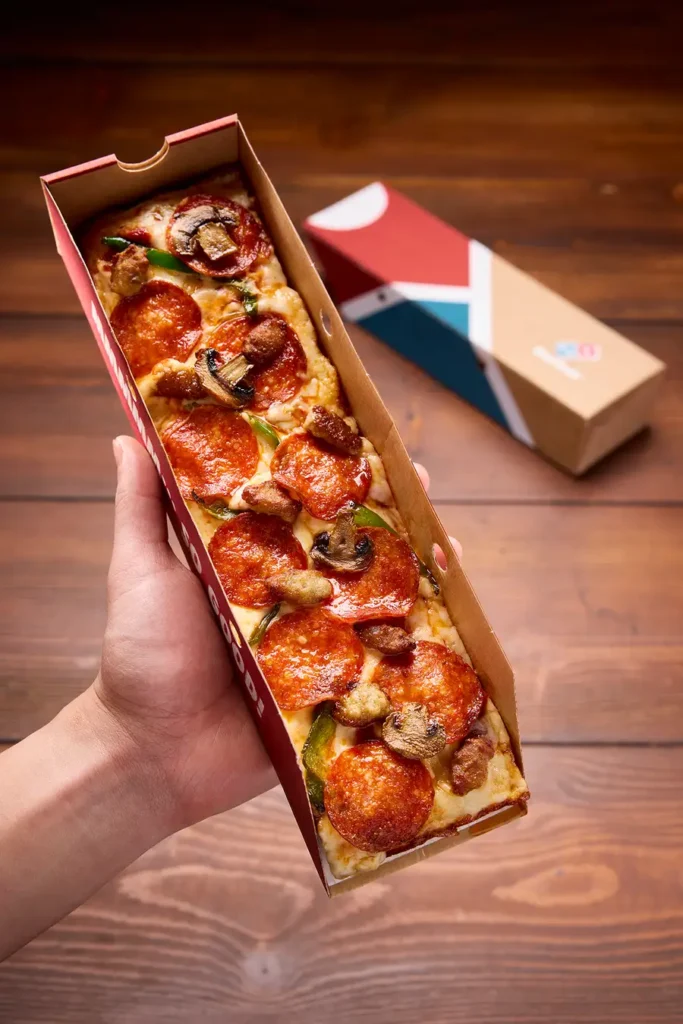 A hand holding a pizza in a box