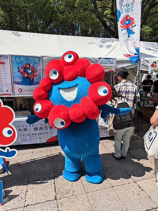 A person in a costume potraying Myakumyaku the mascot character for Expo 2025