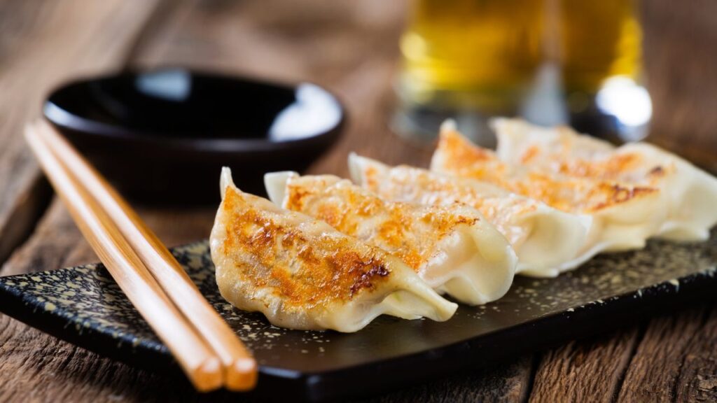 5 gyoza dumplings on a small plate along side a pair of chopsticks