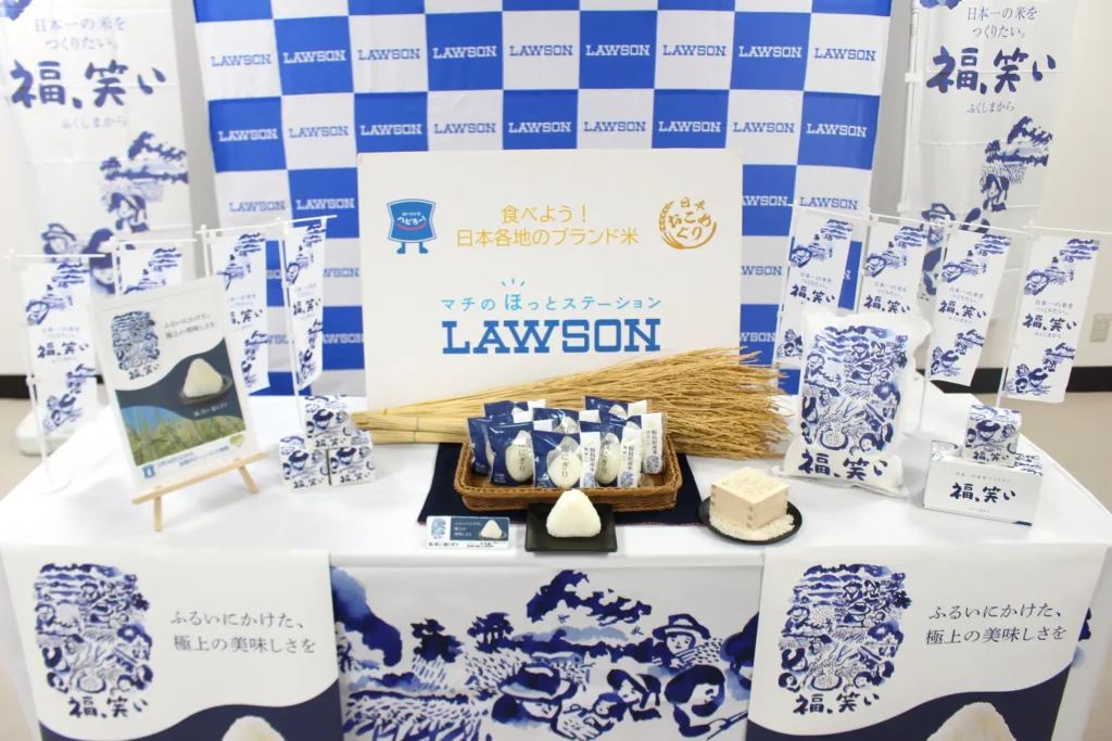 A table holding riceballs, sheafs of harvested rice and Lawson signs