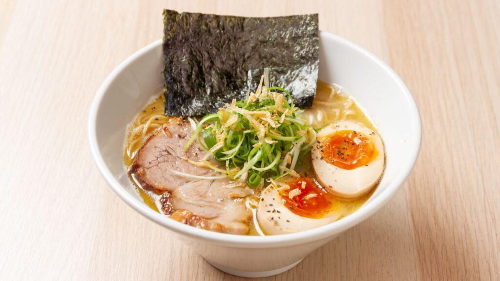 A bowl of ramen topped with pork, seaweed, eggs and onions