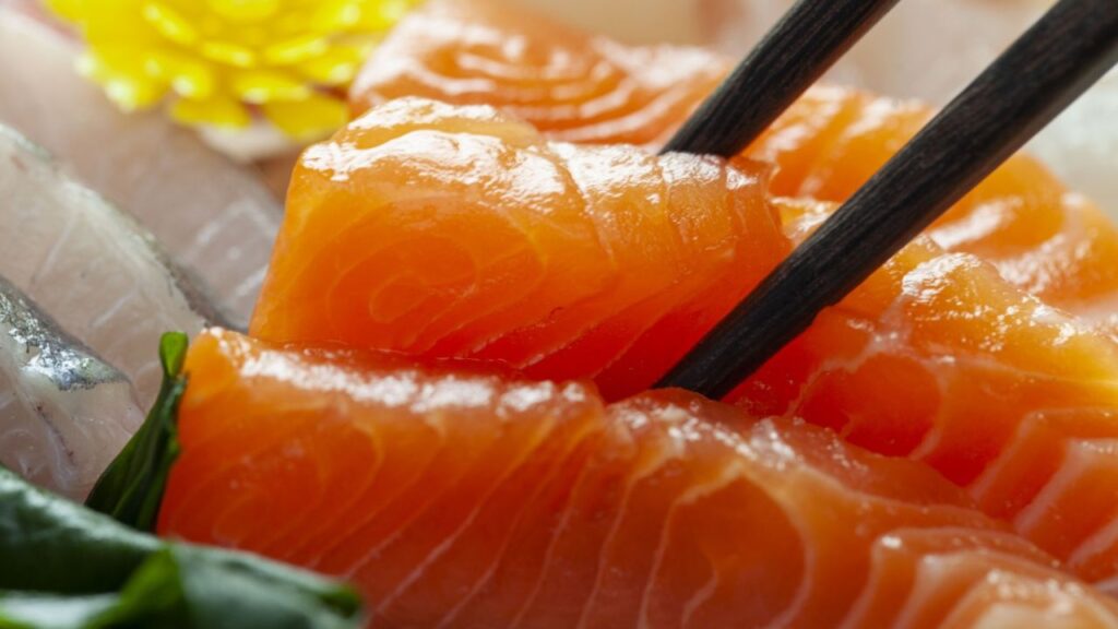 Salmon sashimi being picked up by a chopstick