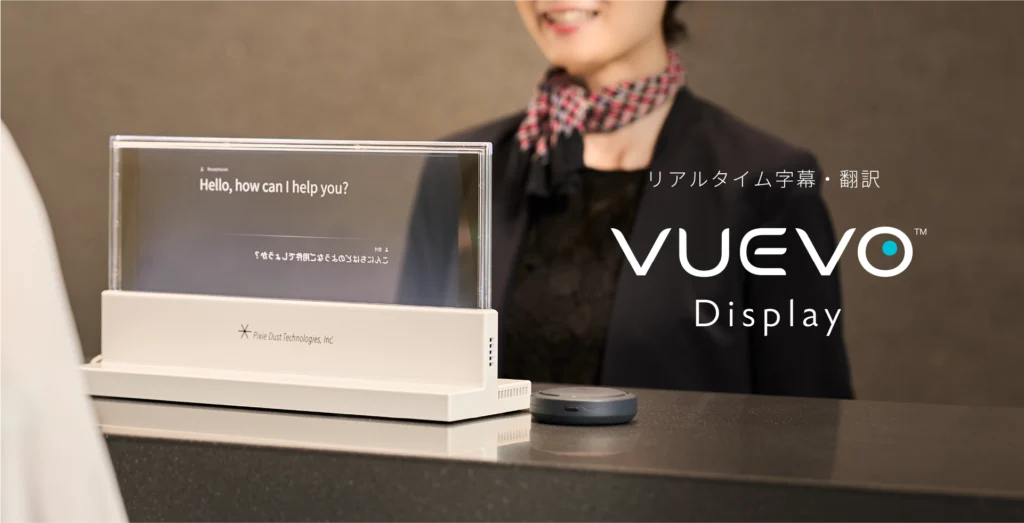 A woman standing behind a screen showing an English translation of a Japanese phrase