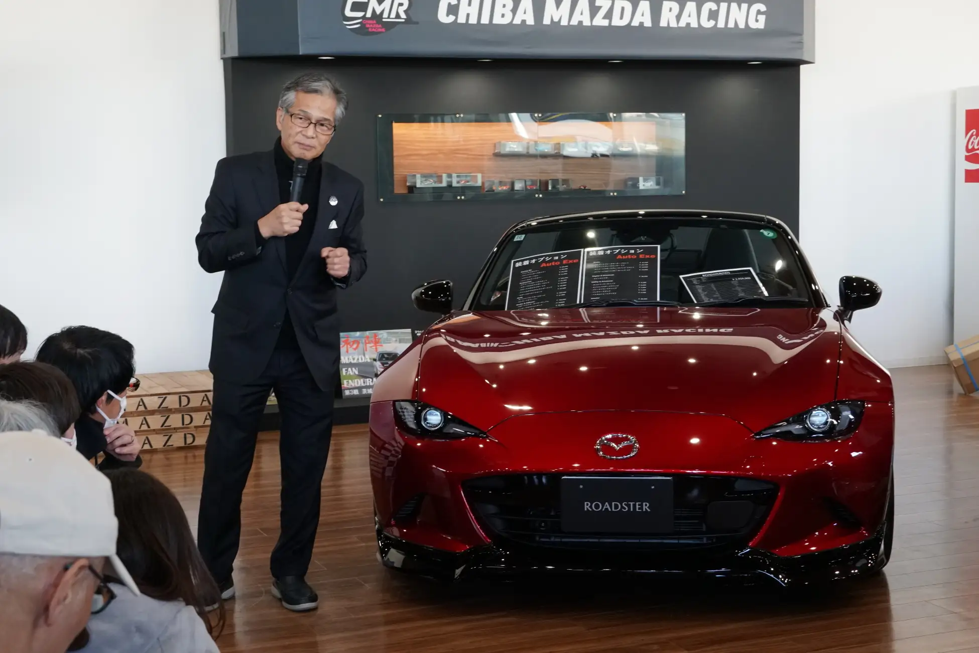 A man holding a microphone standing next to a car A man holding a microphone standing next to a car